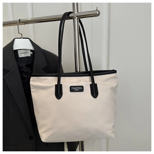 Detail of cream tote bag with black contrast trim and logo patch on fabric texture