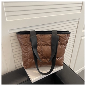 Close-up of brown quilted tote bag showing padded texture and black woven handles