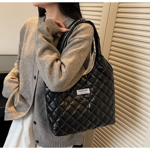 Detail of black quilted puffer bag with white slogan label worn over gray sweater