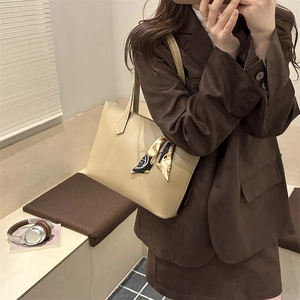 Chic beige tote bag with decorative scarf carried by a woman in a brown suit