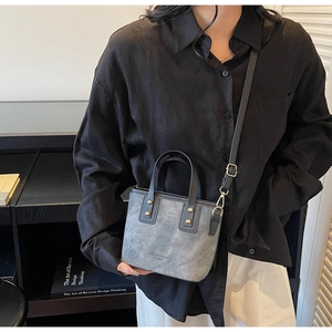 Detail of grey bucket bag featuring gold rivets and crossbody strap in a lifestyle setting