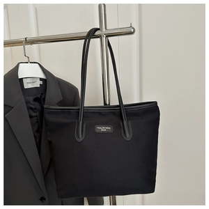 Detail of a black tote bag in durable nylon with brand leather label and slim straps