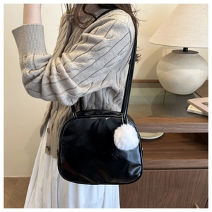 Close-up of black glossy shoulder bag with a fluffy white pompom charm on a model