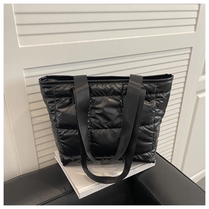 Detail of black quilted puffer tote bag with glossy nylon texture on a seat