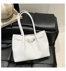 Detail view of woven leather tote bag with silver buckle on minimalist black sofa