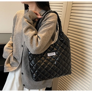 Detail of black quilted puffer tote bag with Fashion Instinct label worn by model