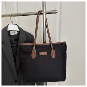 Detail of black tote bag with brown leather handles and brand tag on a suit display