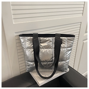 Detail of silver quilted tote bag with metallic finish and black woven shoulder straps