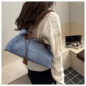 Détail du sac cabas bleu à motif léopard avec bandoulières marron sur un pull blanc