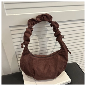 Détail d'un sac cabas en velours marron avec une anse plissée sur un livre blanc