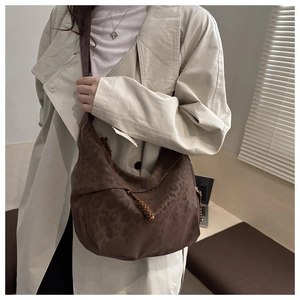 Détail du sac hobo avec imprimé léopard marron et pompon tressé sur texture daim