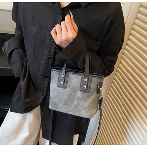 Detail of grey textured bucket bag with black leather trim and gold studs on a model