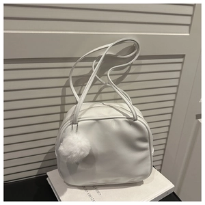 Detail of white textured shoulder bag with plush ball charm on minimalist white background
