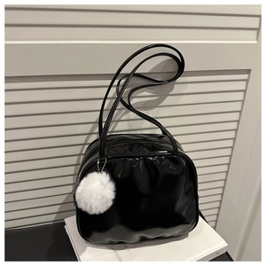 Close-up of black patent leather bag with a white fuzzy pompom charm on white background