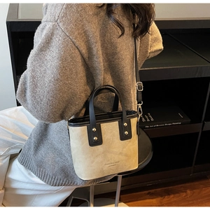 Detailed view of beige suede bucket bag with gold studs and black strap worn by a model