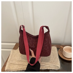Detail of burgundy leopard print shoulder bag with vibrant red canvas strap on a table