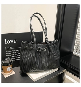 Detailed view of the black herringbone woven texture and decorative buckle on a tote bag
