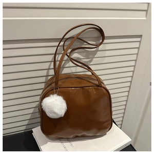 Detailed view of brown glossy shoulder bag with white fluffy charm on white books