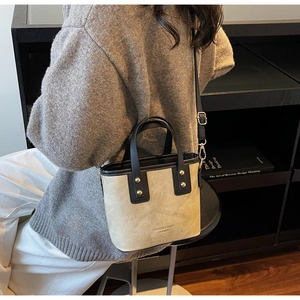Detail of a beige suede bucket bag with black leather straps and gold rivet accents