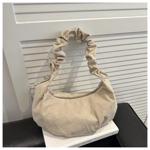 Détail du sac croissant beige avec poignée plissée et tissu texturé sur des livres