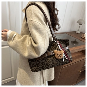 Detail of leopard print tote bag featuring brown leather straps and a plush bear pendant