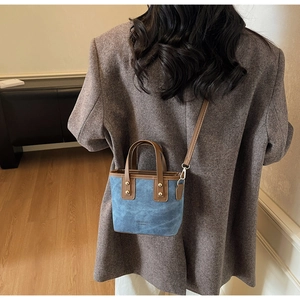 Detail of vintage denim blue bucket bag with brown leather handles worn by a model