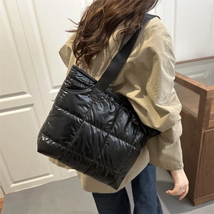 Large black quilted tote bag with shiny finish shown on shoulder in a casual lifestyle setting
