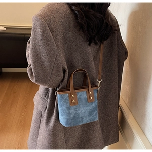 Detail of blue denim style bucket bag with brown leather strap worn on a vintage blazer