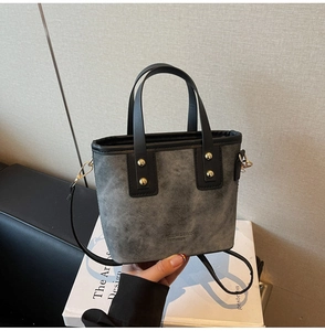 Detail of grey textured bucket bag with leather trim and gold metal rivet accents