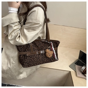 Deep brown leopard print tote bag with leather straps and bear charm in urban setting