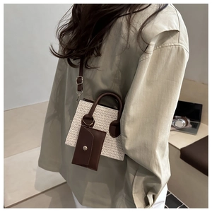 Detail view of beige woven crossbody bag with brown leather accents and hanging coin purse