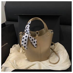 Close-up of beige bucket bag with litchi texture and polka dot silk scarf on handle