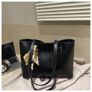 Détail d'un sac cabas noir avec coutures blanches et foulard en soie fleurie sur la poignée