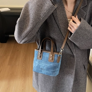 Chic blue denim bucket bag with brown leather trim and rivets, styled with a grey coat