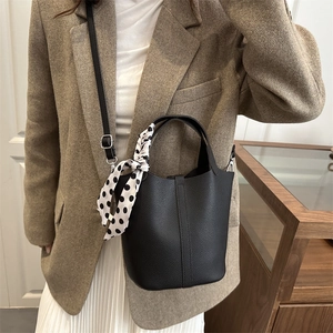 Chic black litchi texture bucket bag with polka dot scarf on a model side profile