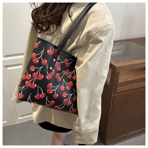 Détail du sac cabas noir avec imprimé cerises et logo doré porté à l'épaule