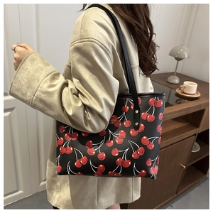 Gros plan d'un grand sac cabas en cuir noir à motif cerises porté par un mannequin