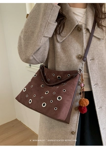 Detail of a brown suede crossbody bag with silver eyelets and a colorful plush charm