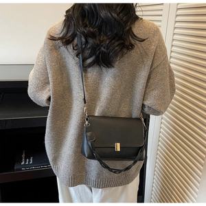 Detail of black matte crossbody bag with gold lock buckle and dual straps on a model