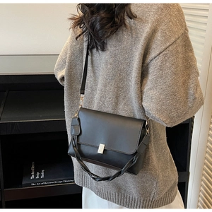Detail of black leather crossbody bag with silver buckle and braided handle strap