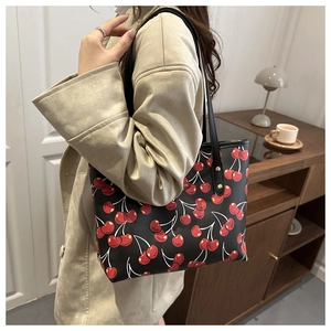Sac fourre-tout noir à motif cerise rouge porté à l'épaule dans un décor chaleureux