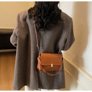 Detail of caramel leather crossbody bag with golden clasp and braided handle detail