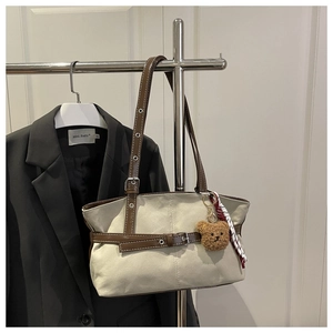 Detail of beige canvas and brown leather tote bag with plush bear charm and silk scarf