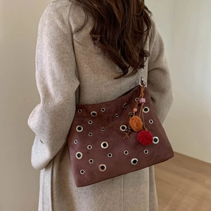 Brown suede hobo bag with silver eyelets and colorful pompom on model in beige coat