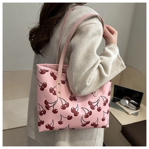 Détail du cabas rose à imprimé cerise avec clous dorés porté par un mannequin en intérieur