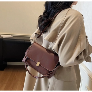 Detailed view of a retro dark brown leather crossbody bag styled on a beige trench coat