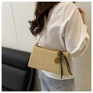 Dettaglio borsa a tracolla intrecciata beige con foulard di seta e ciondolo in metallo
