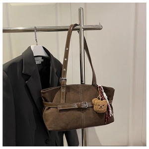 Detail of dark brown suede shoulder bag featuring a silver buckle and cute bear charm