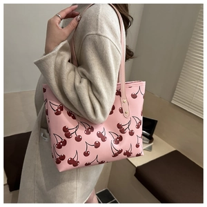 Détail d'un sac cabas rose avec motif cerise porté sur un manteau beige par une femme