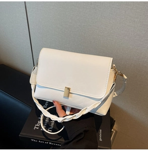Close-up of white minimalist crossbody bag with golden clasp and woven handle detail